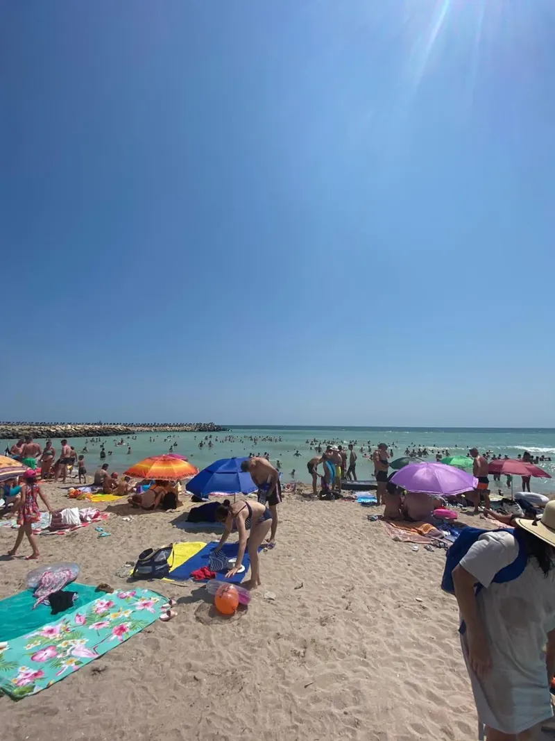 Plaja din Costinești într-o zi de vară, cu apa verde-albastră și oameni pe nisip.